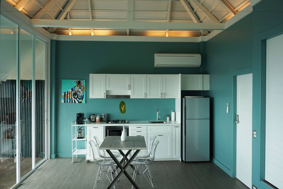 Una cocina moderna con armarios blancos, un refrigerador de acero inoxidable y un comedor con mesa y sillas de vidrio.