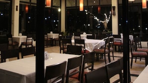 A restaurant with tables and chairs, large windows, and hanging pendant lights. - Aekpailin River Kwai Resort Kanchanaburi (Kanchanaburi)