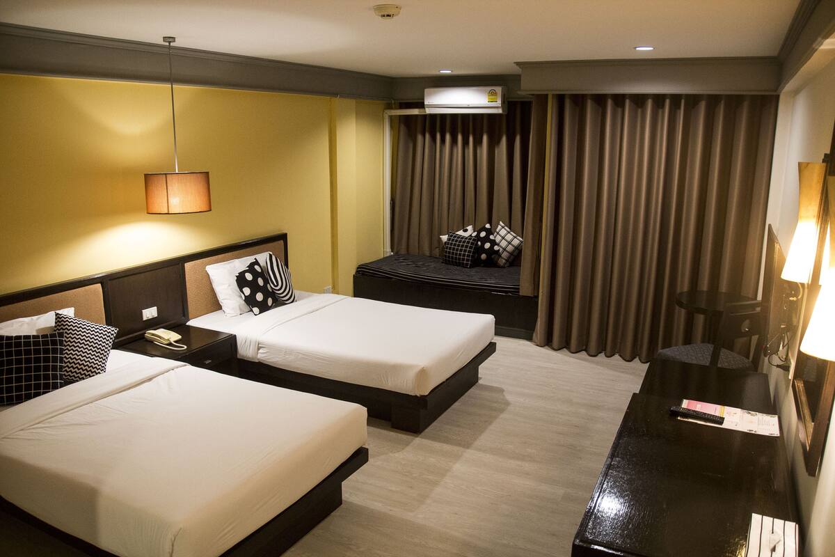 Une chambre d’hôtel avec deux lits, un bureau, une chaise, un appareil de climatisation et un rideau.
