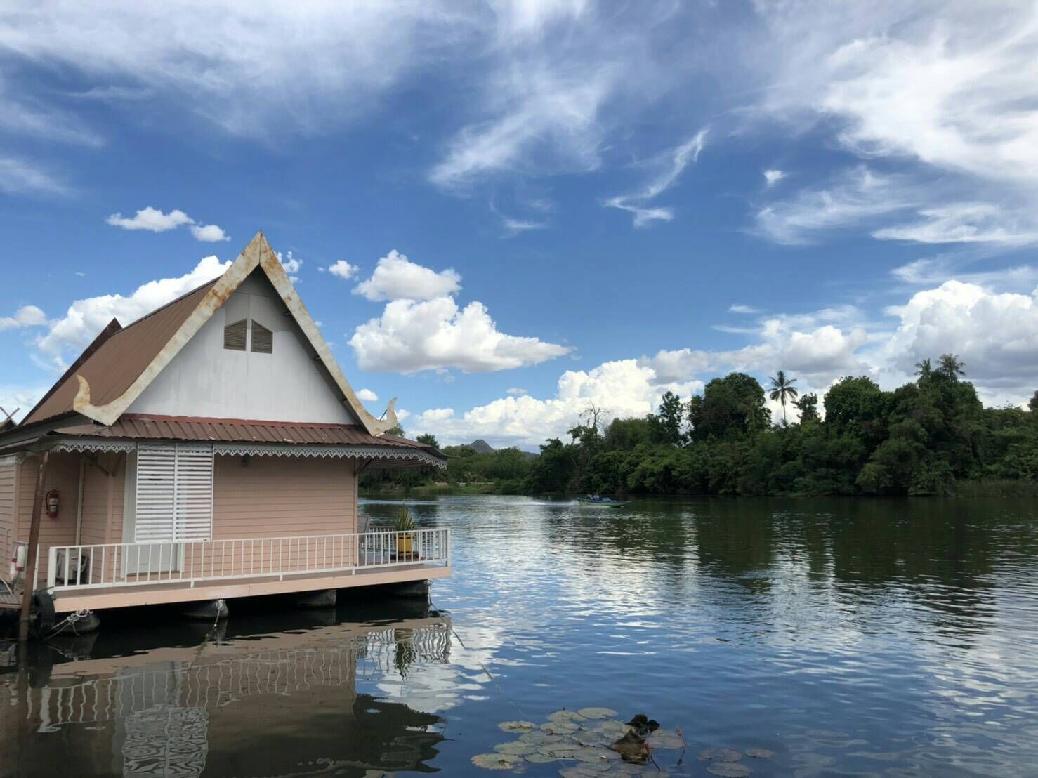 Una casa flotante con balcón, navegando en un río tranquilo rodeado de abundante vegetación.