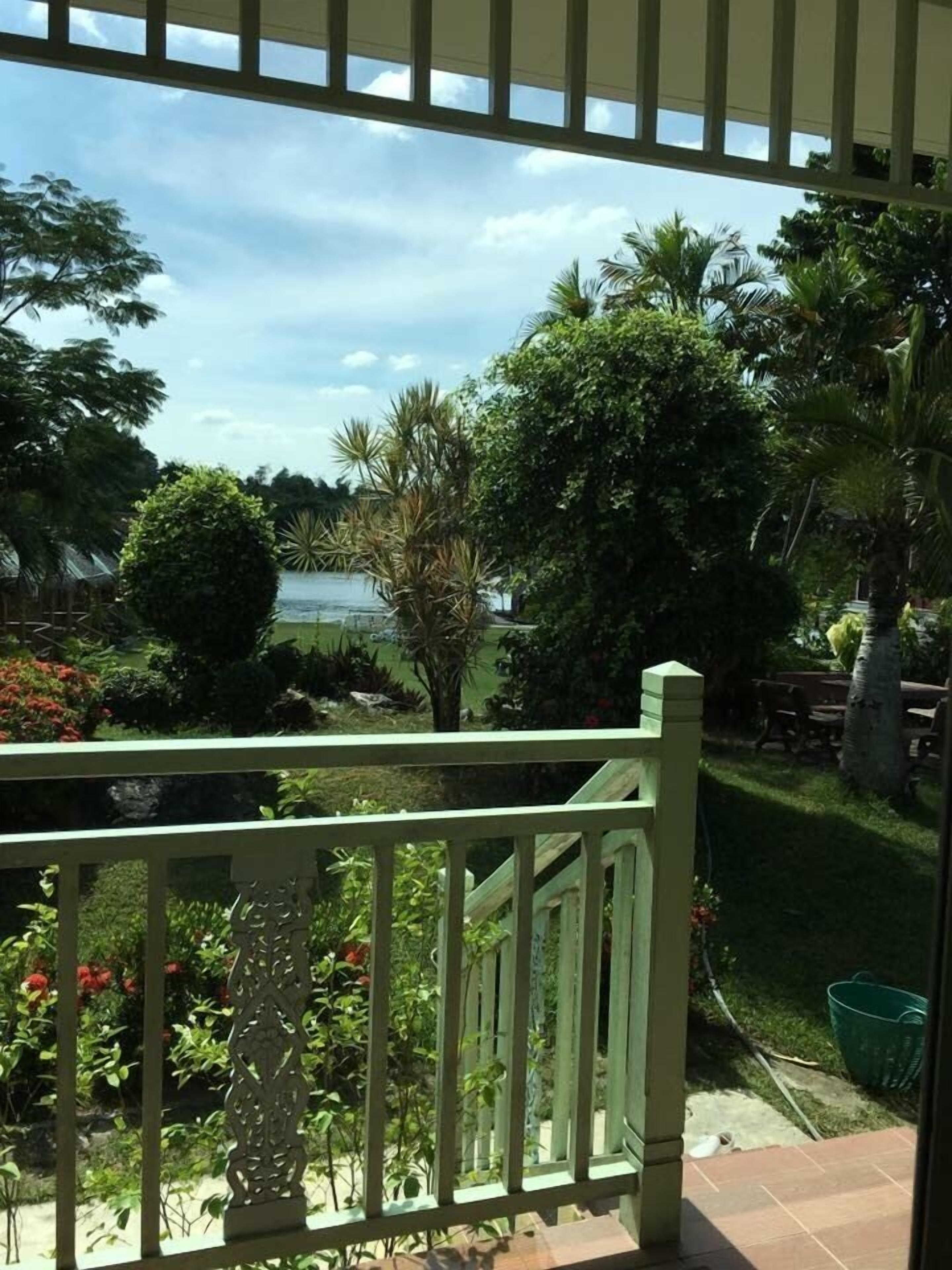 Vista de uma varanda com guarda-corpo, sobre um jardim com diversas plantas e um corpo de água.