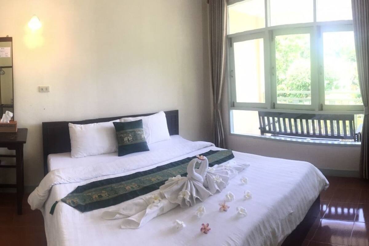 Ein Hotelzimmer mit Bett, Schreibtisch, Stuhl, Spiegel und einem Fenster mit Blick ins Grüne.