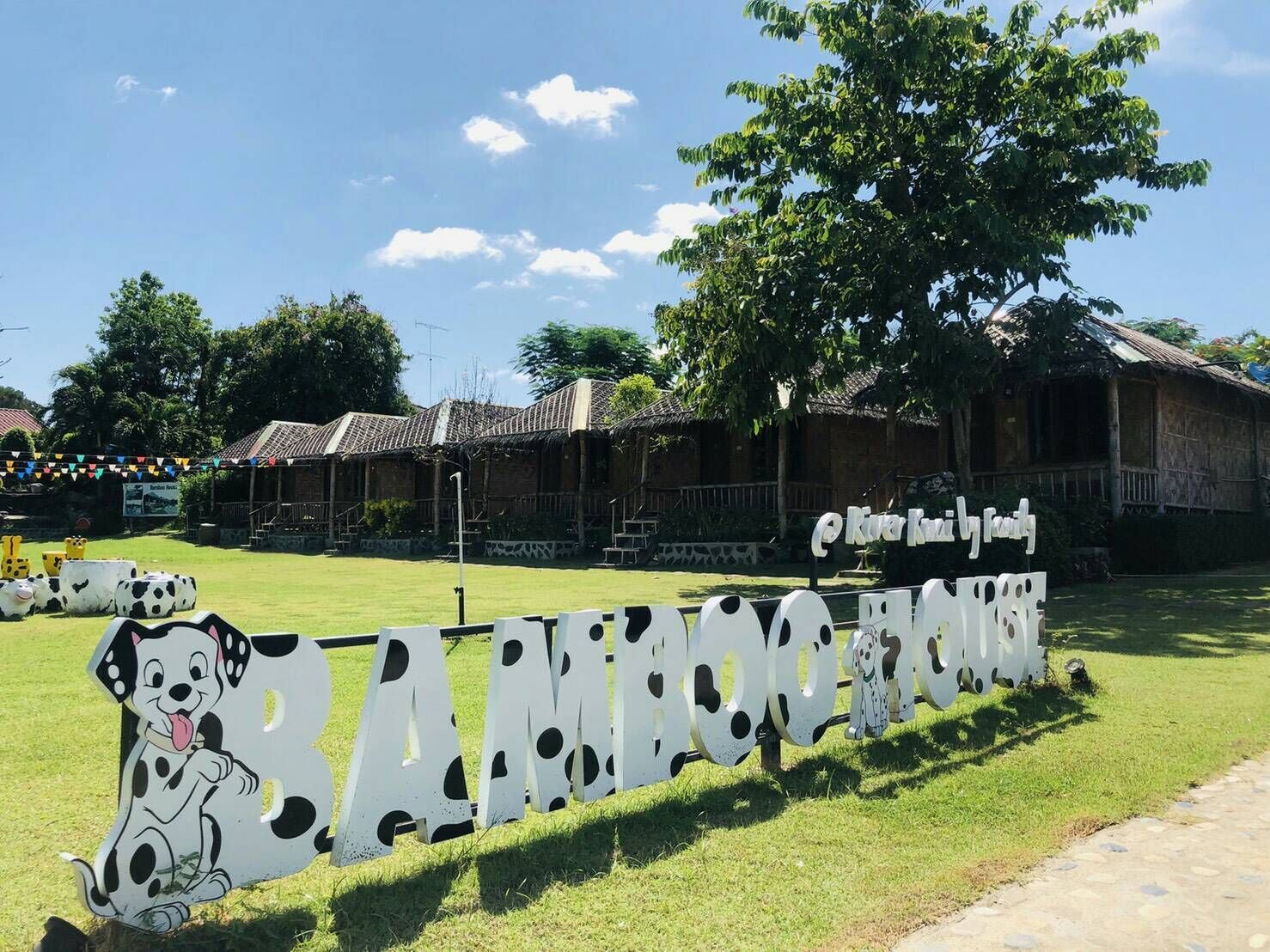 A sign with a cow and a dog, and a building with a thatched roof in the background.