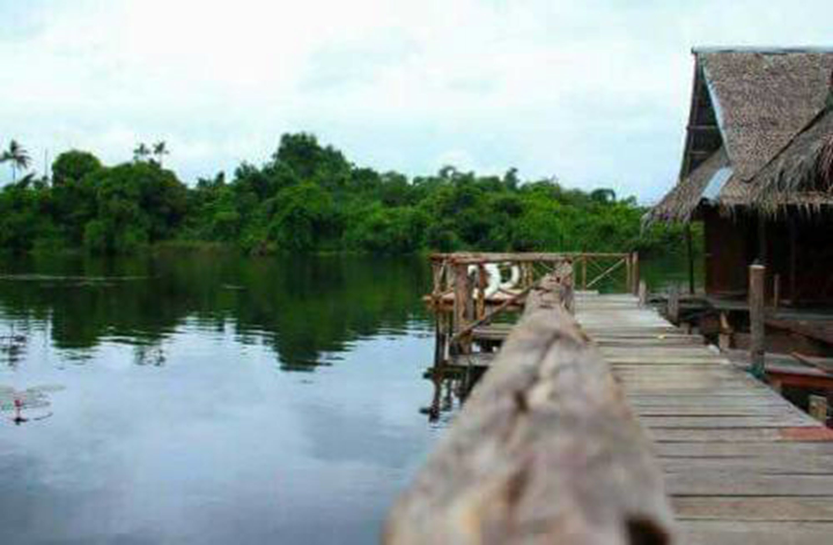 A wooden pier extending into calm water, with a thatched-roof structure on the right.
