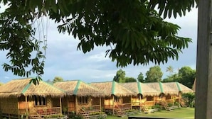 Un complexe hôtelier doté de bungalows aux toits de chaume, d’une terrasse en bois avec des tables et des chaises, et d’une pelouse bien entretenue.
