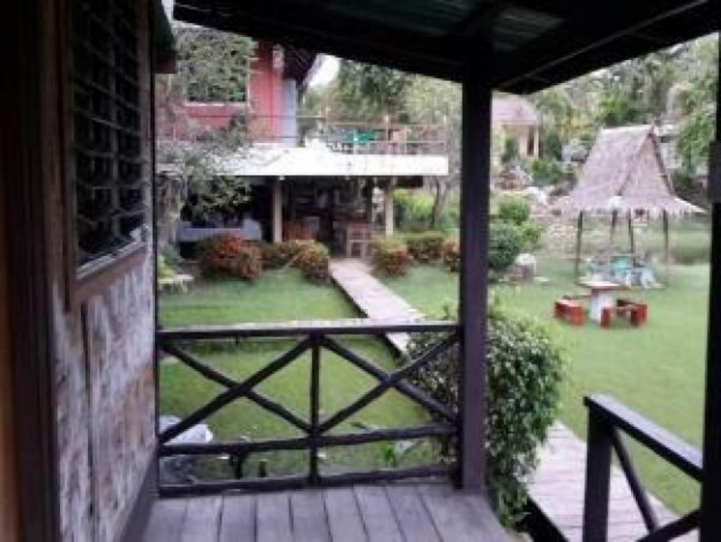A wooden deck with a railing, a thatched structure, and a small table with chairs.