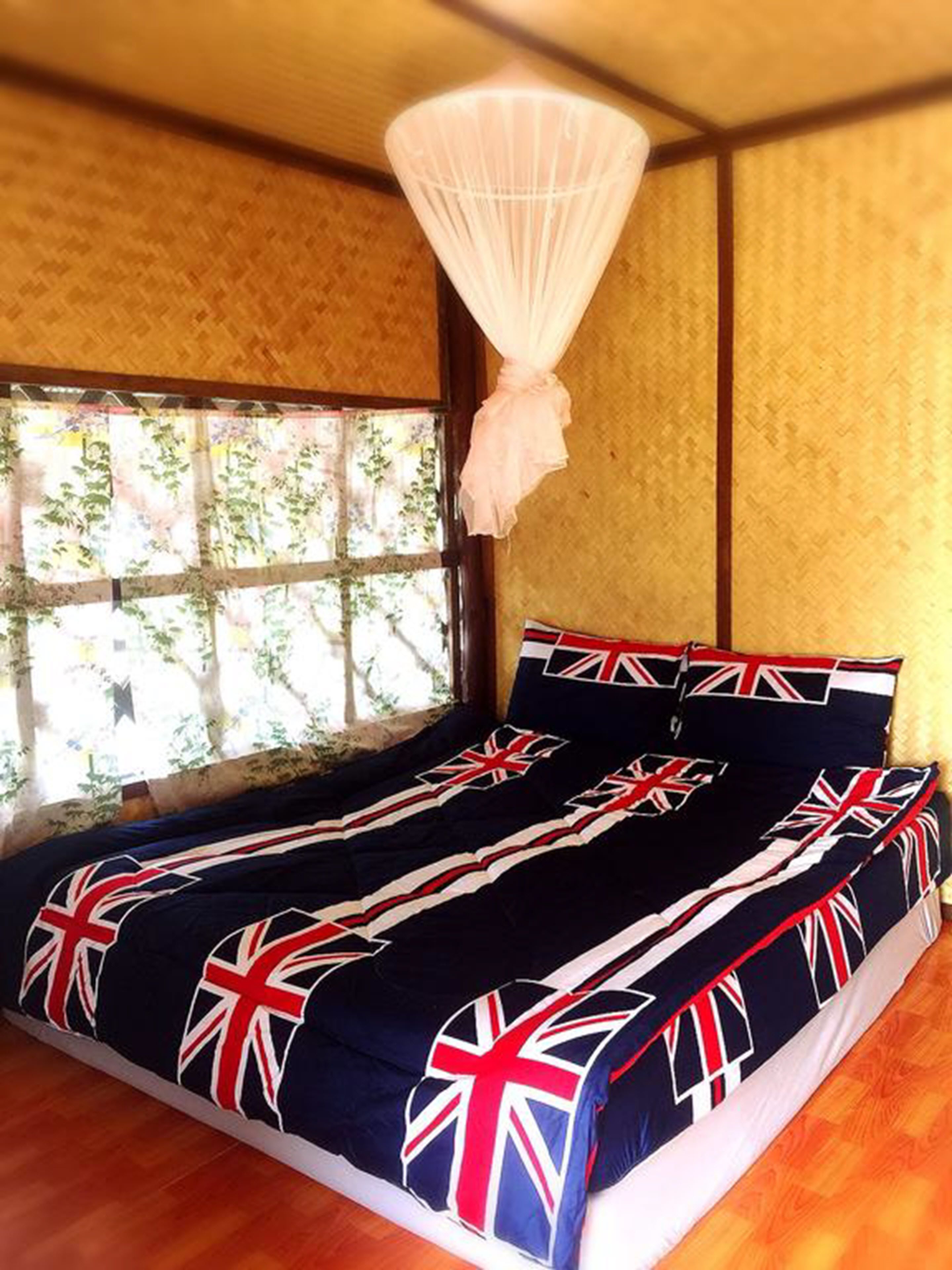 Uma cama com design da Union Jack, uma janela com vista para o verde e piso de madeira.