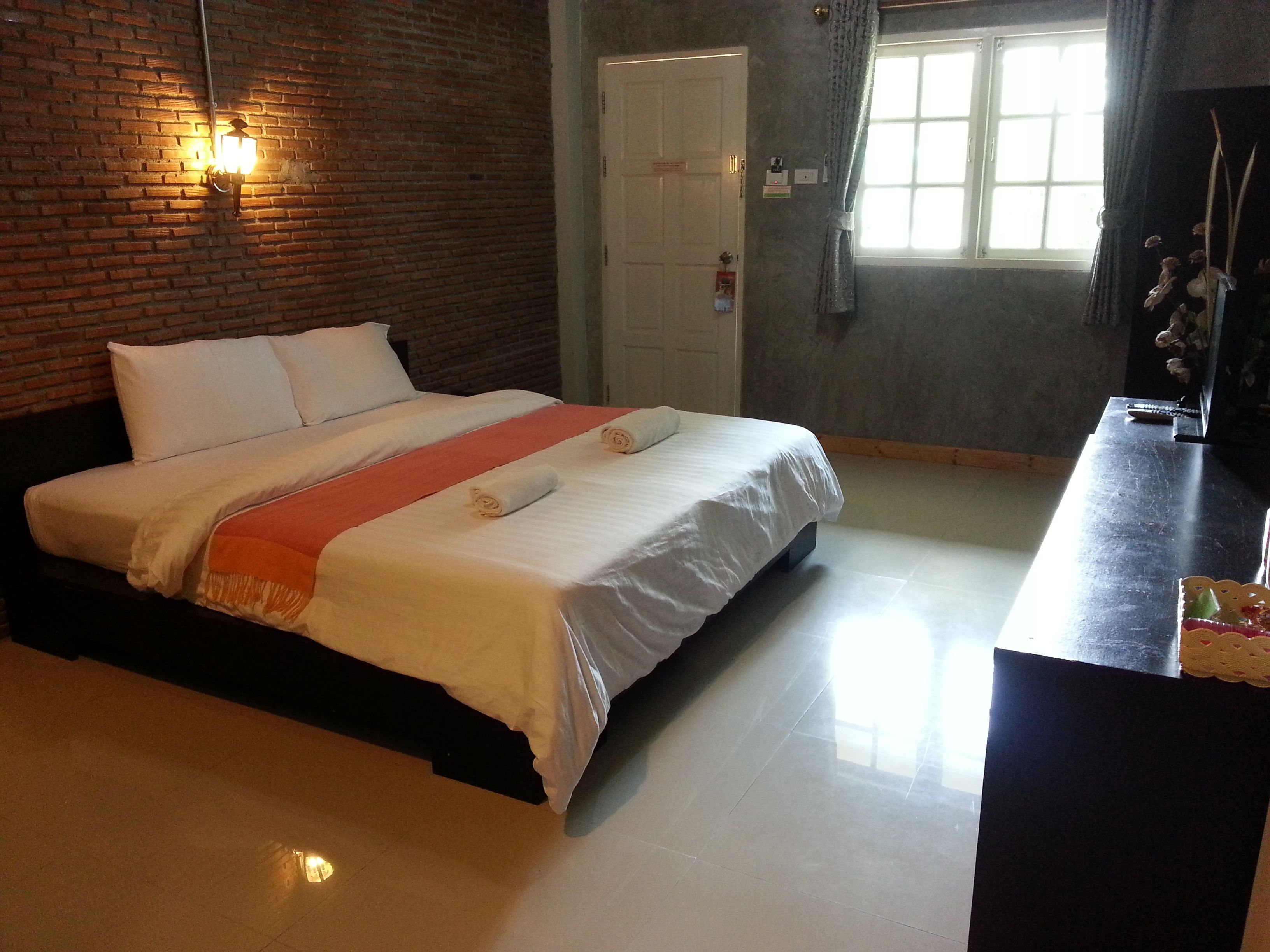 Quarto de hotel com parede de tijolos, cama com roupa branca, mesa de cabeceira e janela com cortinas.