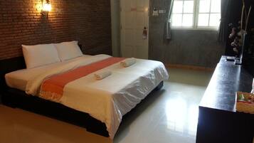 Quarto de hotel com parede de tijolos, cama com roupa branca, mesa de cabeceira e janela com cortinas.