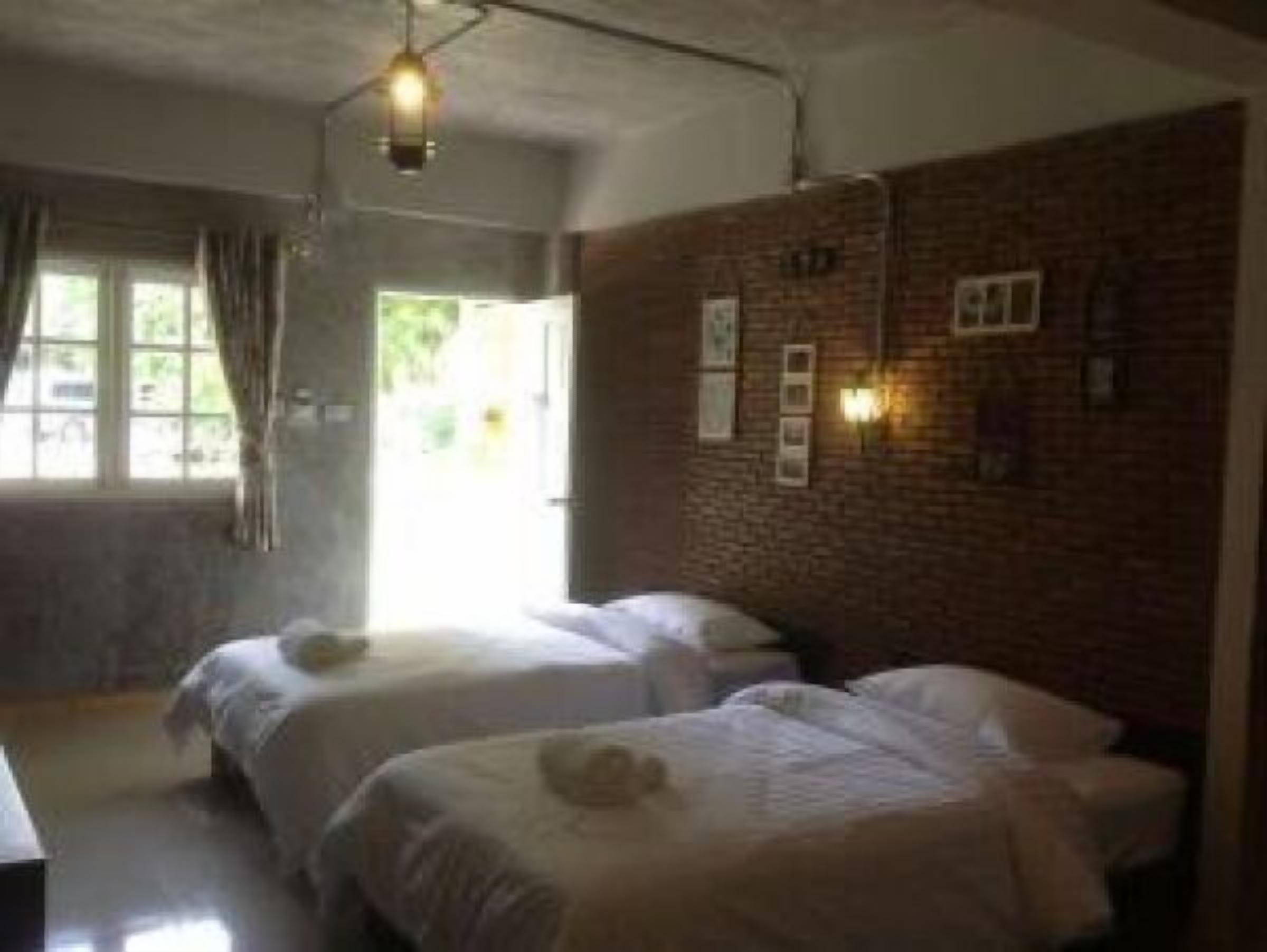 A room with two beds, a brick wall, and a window with curtains.