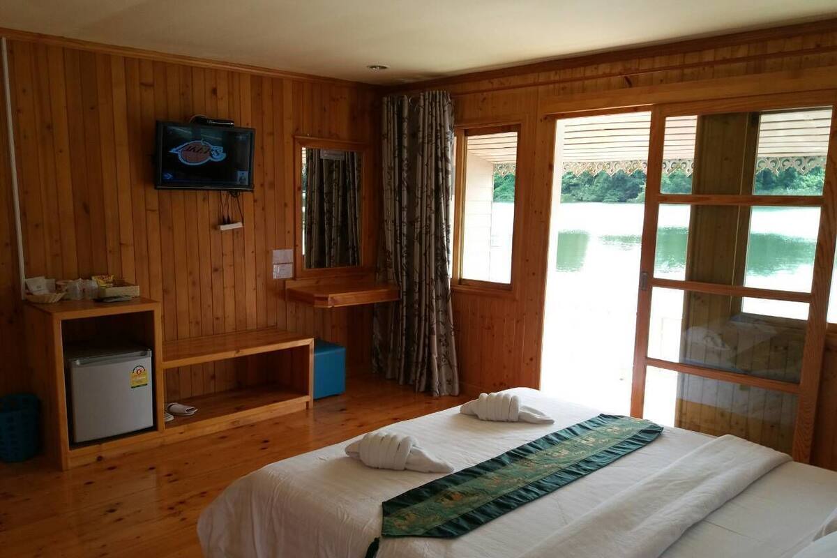 Ein Zimmer mit Holzwänden, einem Bett, einem Fernseher, einem kleinen Schreibtisch und einem Fenster mit Blick auf Grünflächen.