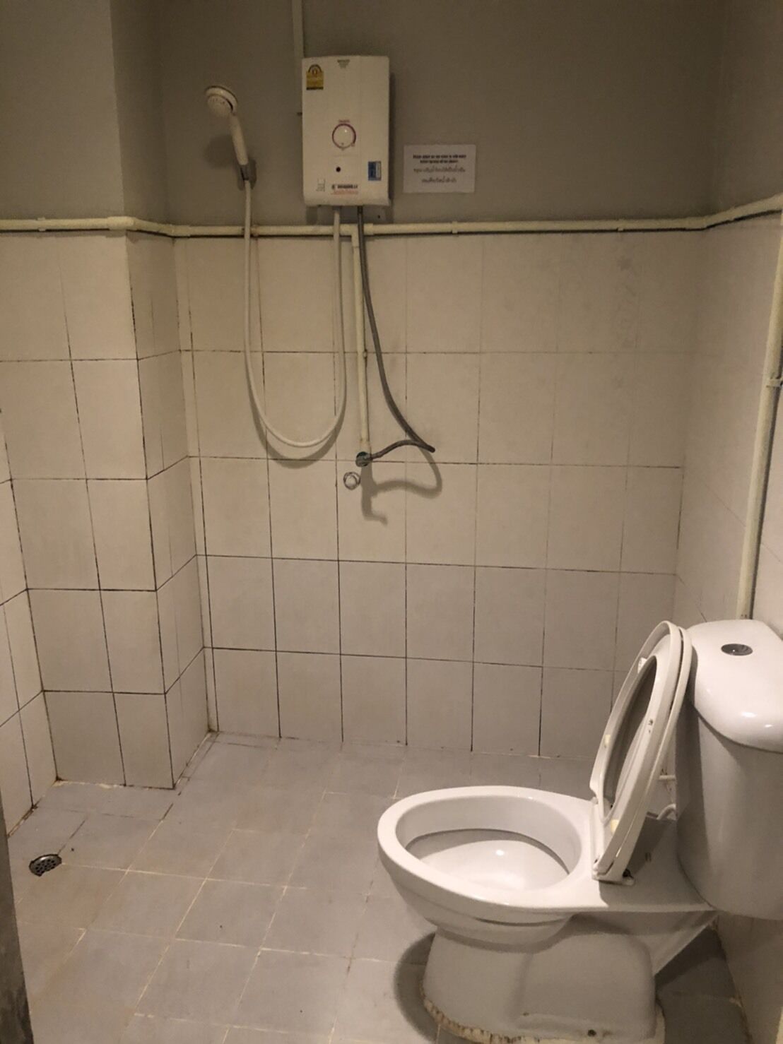 Pieni, laatoitettu kylpyhuone, jossa on wc, suihkupää ja vedenlämmitin.