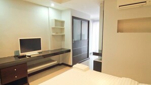 Habitación de hotel con una cama, un televisor en un mueble, un escritorio con una computadora, un espejo y un equipo de aire acondicionado.