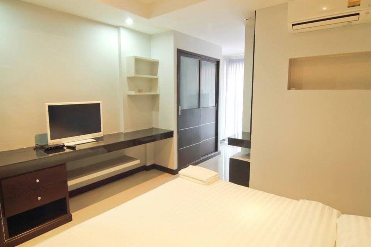 Une chambre d’hôtel comprenant un lit, un téléviseur posé sur un meuble, un bureau avec un ordinateur, un miroir et un appareil de climatisation.