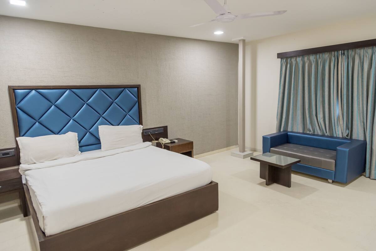 Una habitación de hotel moderna con una cama grande, un sofá, una mesita pequeña y una mesita de noche.