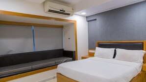 A modern bedroom with a bed, a bench, and a wall-mounted air conditioner. - Ginger Ahmedabad, Satellite (Ahmedabad)