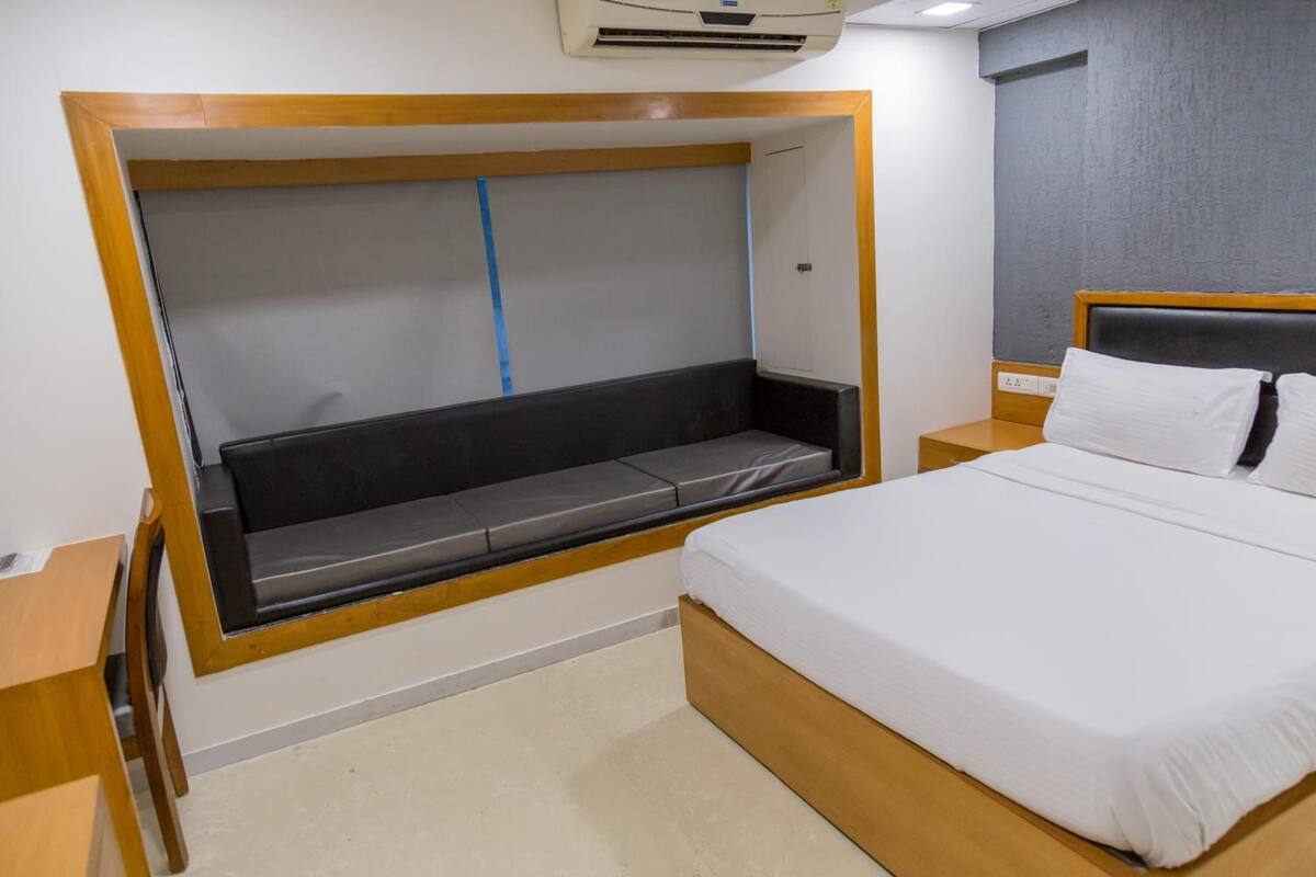 Un dormitorio con cama, un banco empotrado con espacio de almacenamiento, una mesita de noche y un aire acondicionado de pared.