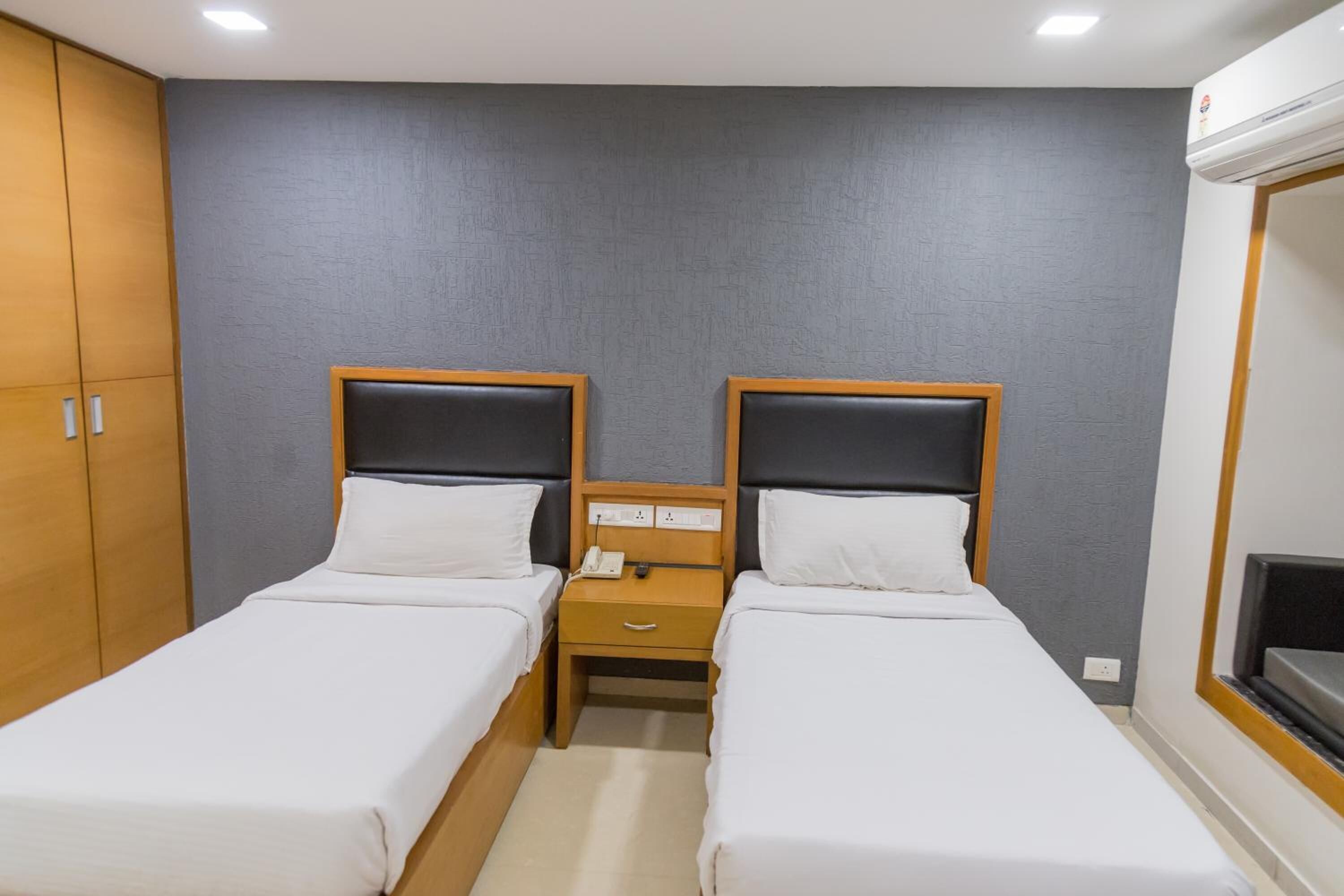 Une chambre d’hôtel avec deux lits simples, une armoire en bois, une table de chevet avec un téléphone et une fenêtre donnant sur un paysage agréable.