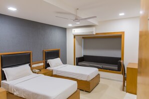 A hotel room with two single beds, a ceiling fan, an air conditioning unit, and a window with a view. - Ginger Ahmedabad, Satellite (Ahmedabad)