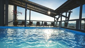 Une piscine à débordement située sur le toit, avec une eau d’un bleu cristallin, entourée de chaises longues et d’une pergola.