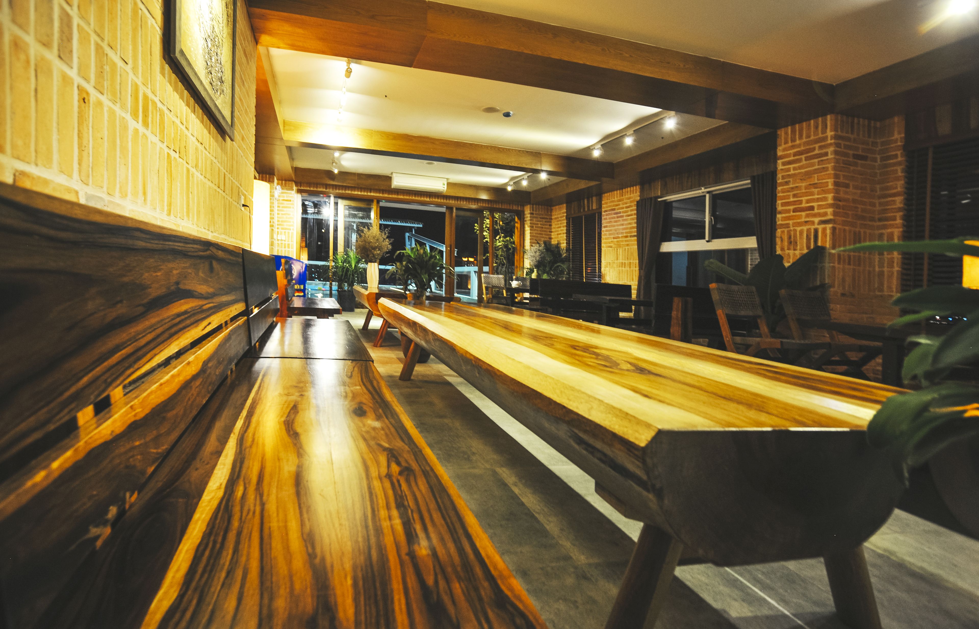 Un largo banco de madera con respaldo alto, una mesa de madera y una pared de ladrillo con una ventana.