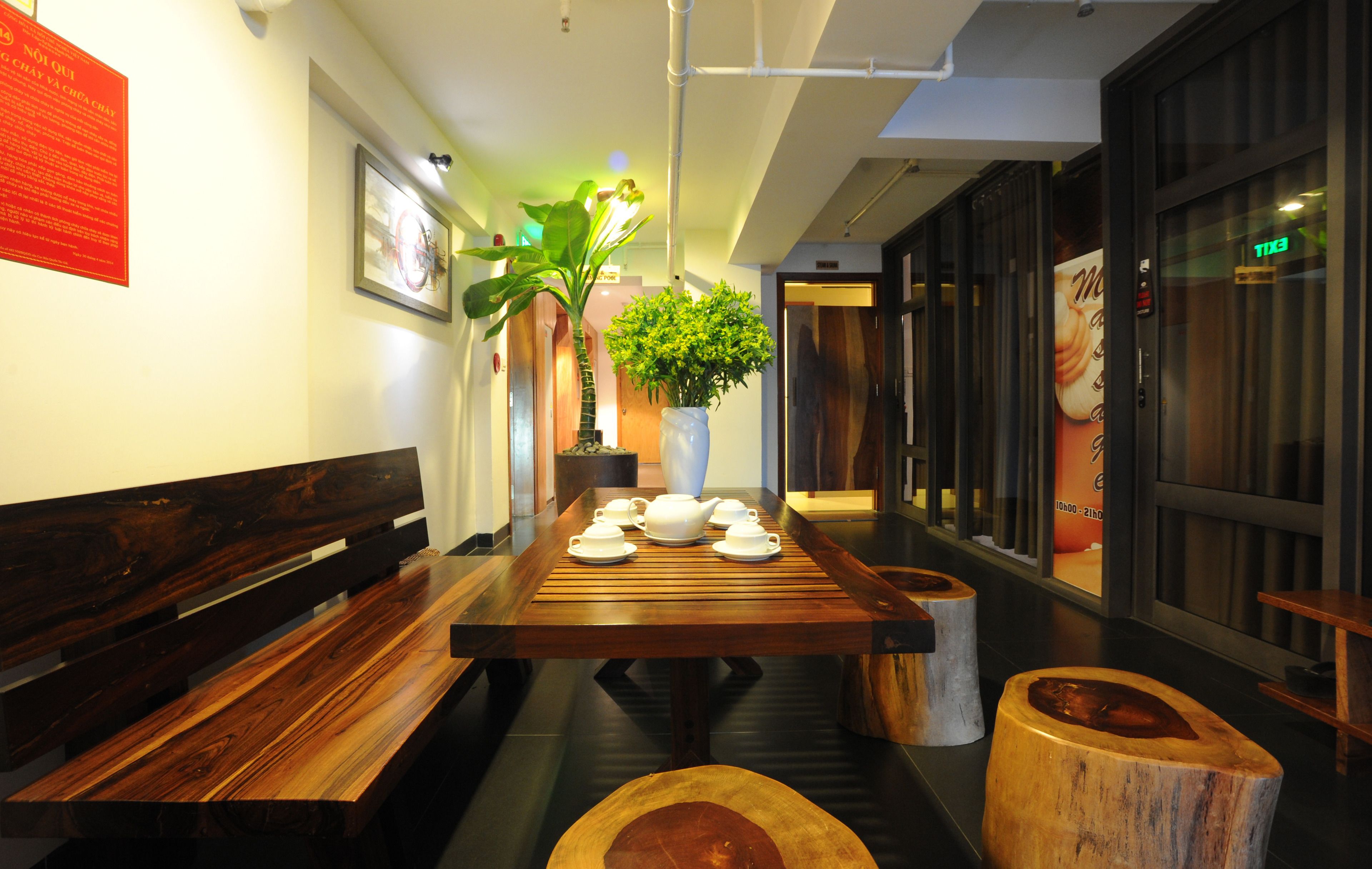 Una mesa de madera con teteras y tazas, un banco y una planta en maceta en un interior moderno.