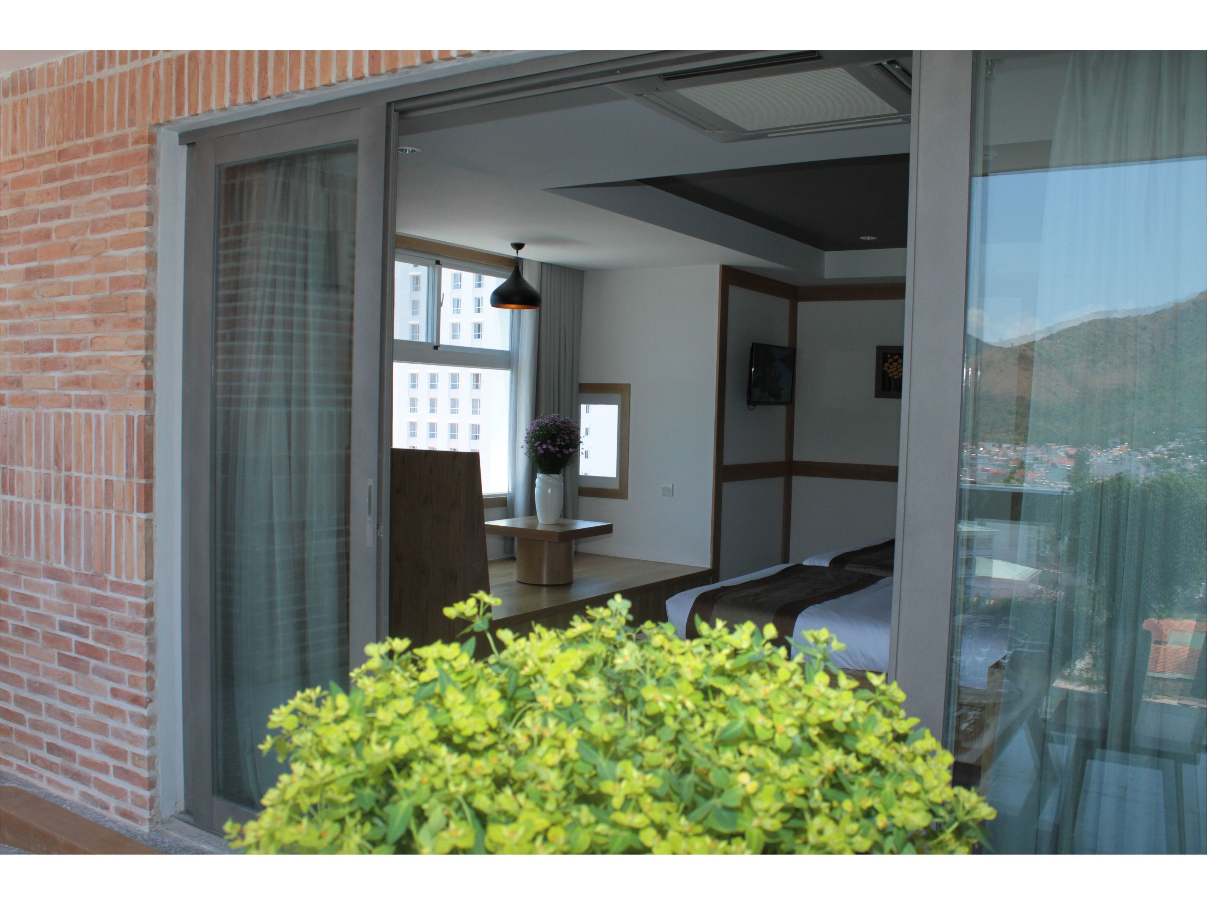A modern room with a large sliding glass door leading to a balcony, a wooden bench, and a small table with a vase of flowers.