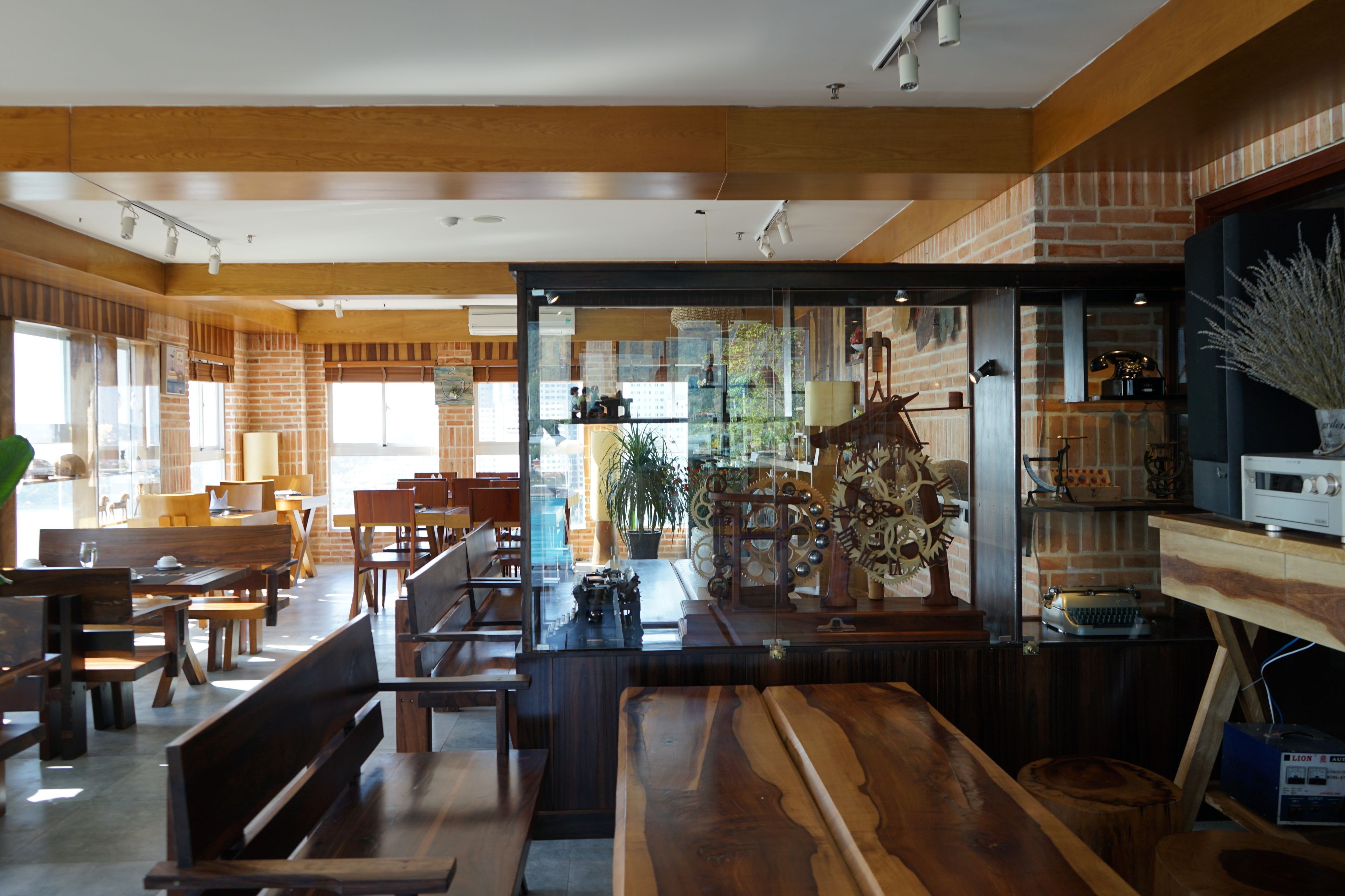 A restaurant with wooden furniture, brick walls, and a glass partition.