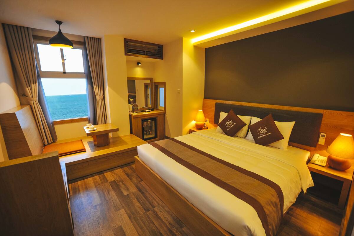 Une chambre d’hôtel avec un grand lit, un bureau, une chaise, une table de chevet et une vue sur la mer.