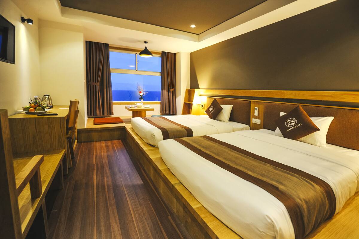 Une chambre d’hôtel avec deux lits, un bureau et une vue sur la mer.