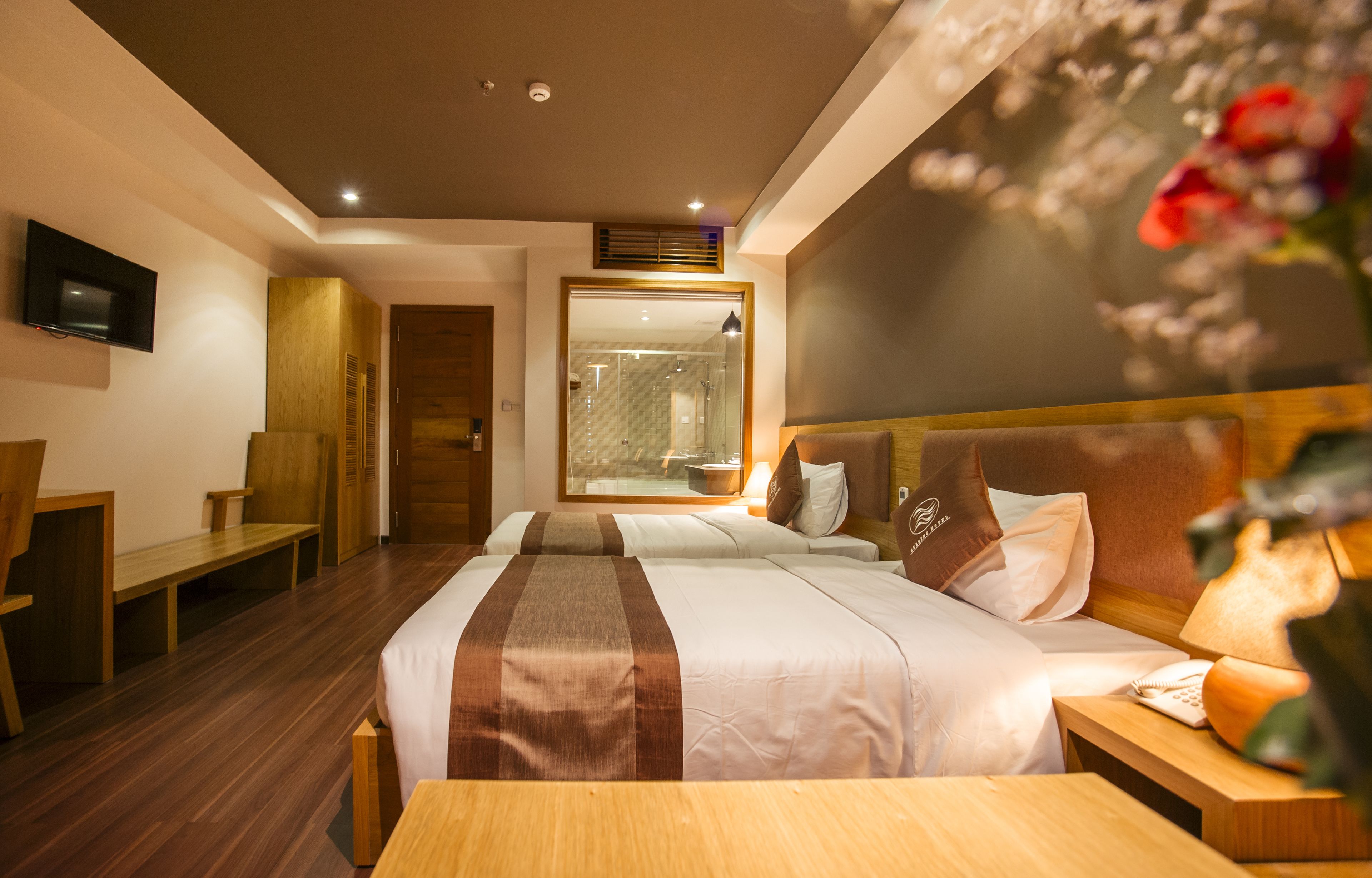 A hotel room with a large bed, a bedside table, a TV mounted on the wall, and a shower area visible through a glass door.