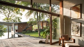 A modern interior with a wooden deck, large windows, and a view of a tropical garden. - Umah Tampih Villa (Ubud)