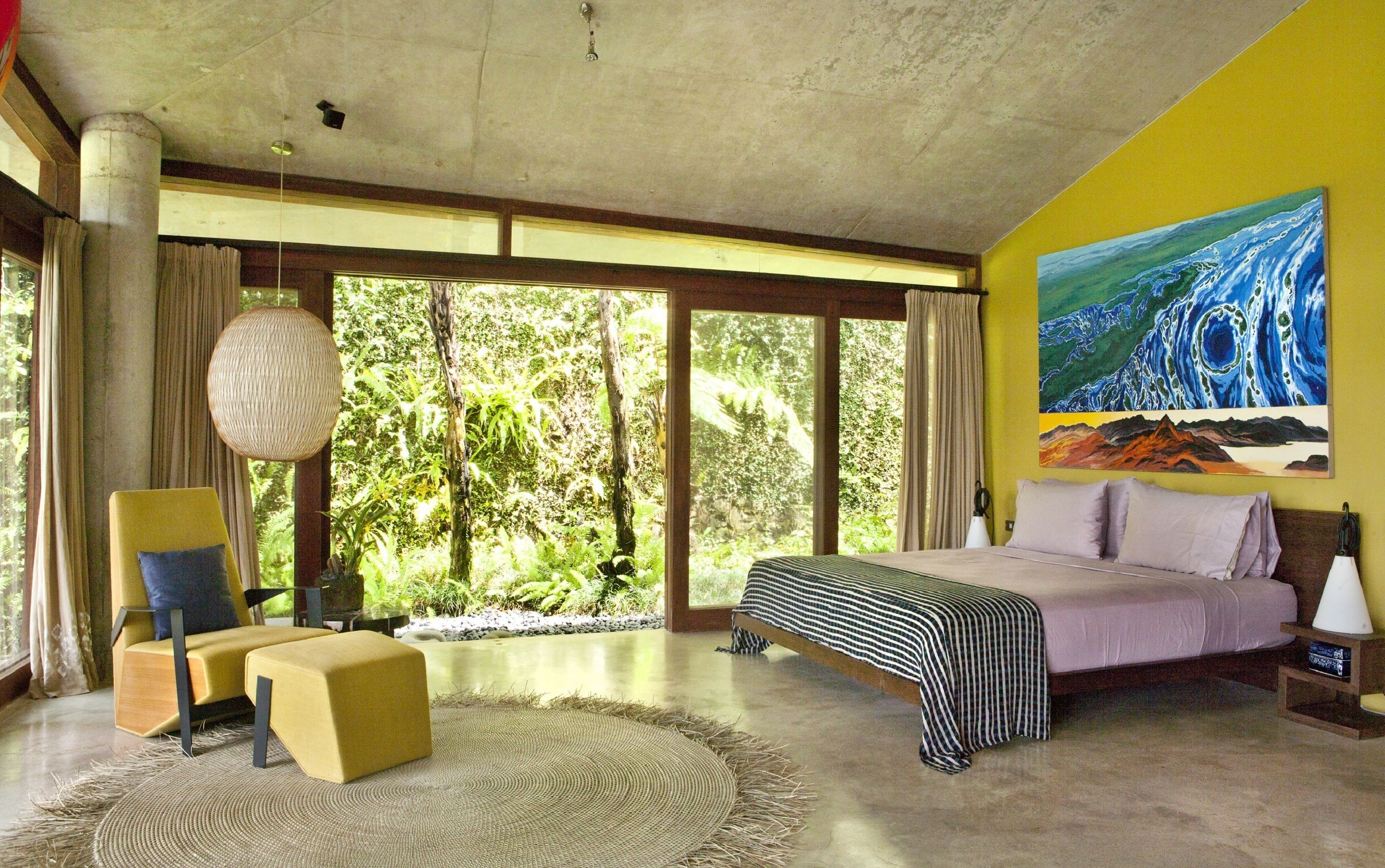 Un dormitorio con una cama grande, un sillón amarillo, una alfombra tejida y un cuadro de un paisaje.