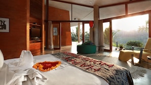 A modern hotel room with a large bed, a ceiling fan, a view of the outdoors, and a balcony with seating. - Umah Tampih Villa (Ubud)