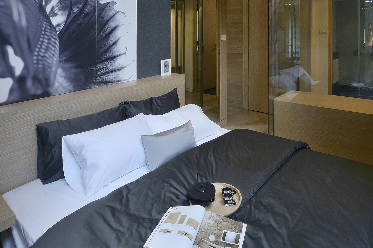 A modern hotel room with a large bed, a wall-mounted artwork, and a glass-enclosed shower area.
