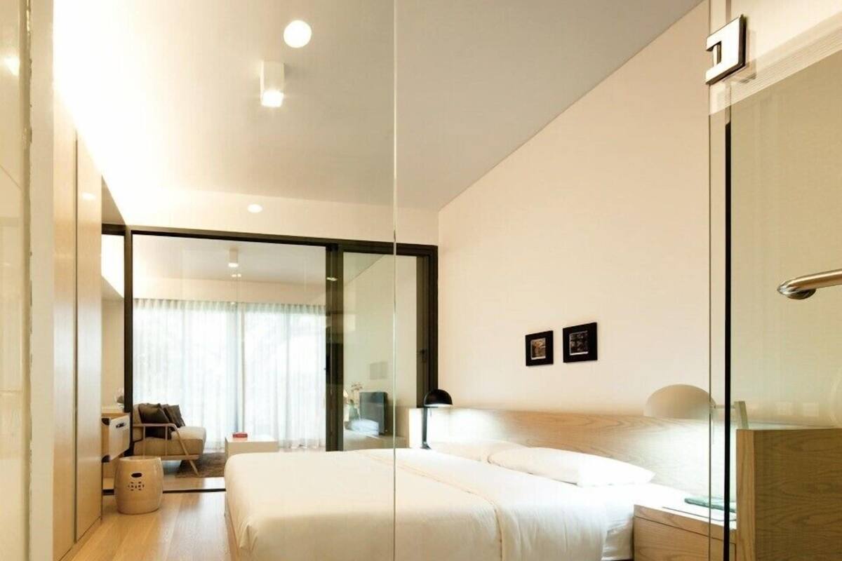 A modern hotel room with a large bed, a glass partition, a desk, and a chair.