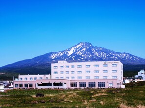 A hotel with a mountain backdrop, featuring a modern building with multiple windows and a flat roof. - Island Inn Rishiri (Rishiri)