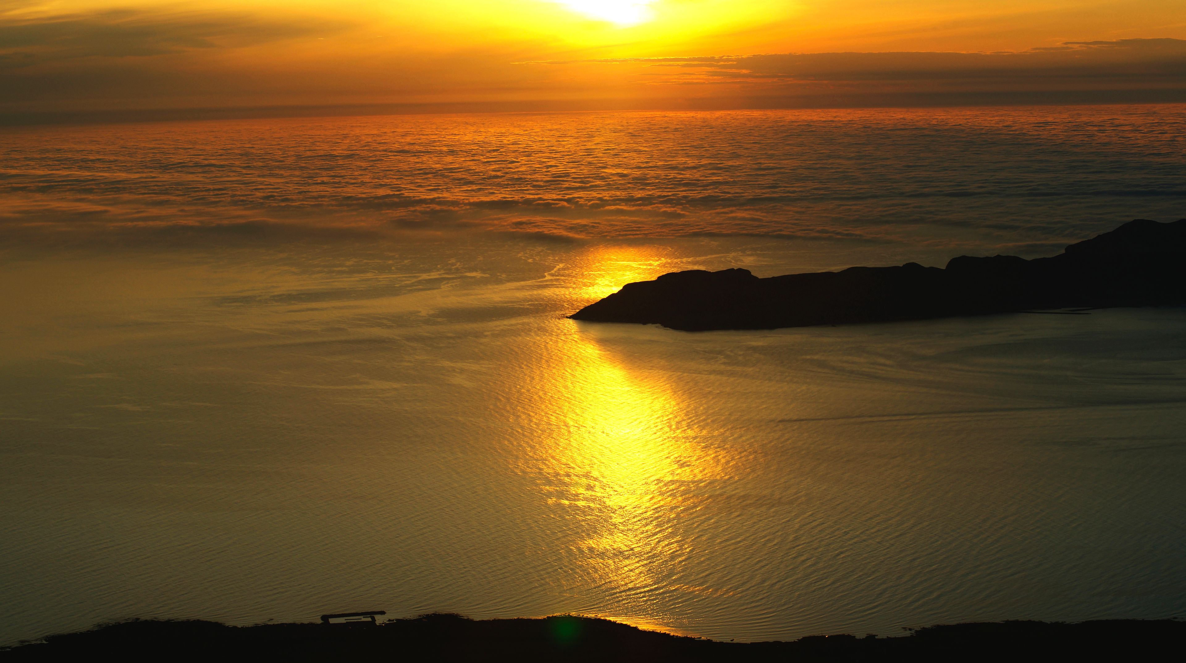 A sunset over a calm sea with a rocky coastline.