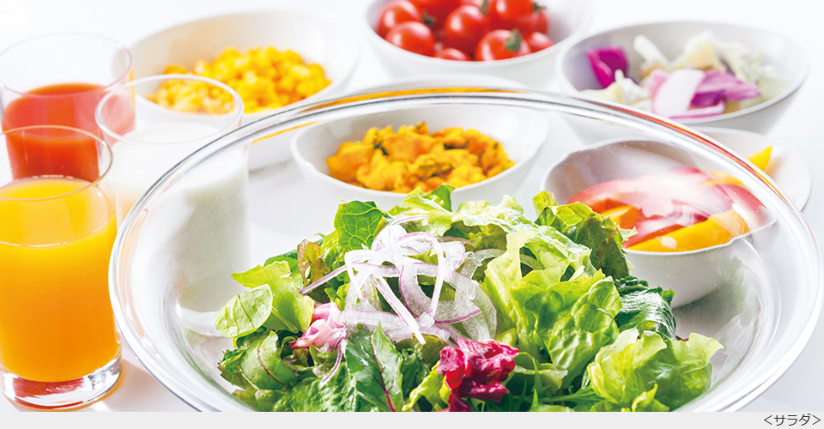 Una mesa con diferentes alimentos, entre ellos una ensalada, tazones de maíz, tomates y un vaso de jugo de naranja.