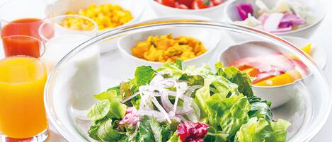 Una mesa con diferentes alimentos, entre ellos una ensalada, tazones de maíz, tomates y un vaso de jugo de naranja.