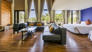 A spacious room with a large bed, a sofa, and a dining table. There are large windows with curtains, a brick wall, and a view of greenery outside. - Southern Sun Homestay North (Hengchun)