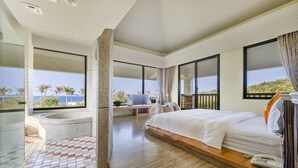 A modern hotel room with a large bed, a bathtub, and a view of palm trees and hills. - Southern Sun Homestay North (Hengchun)