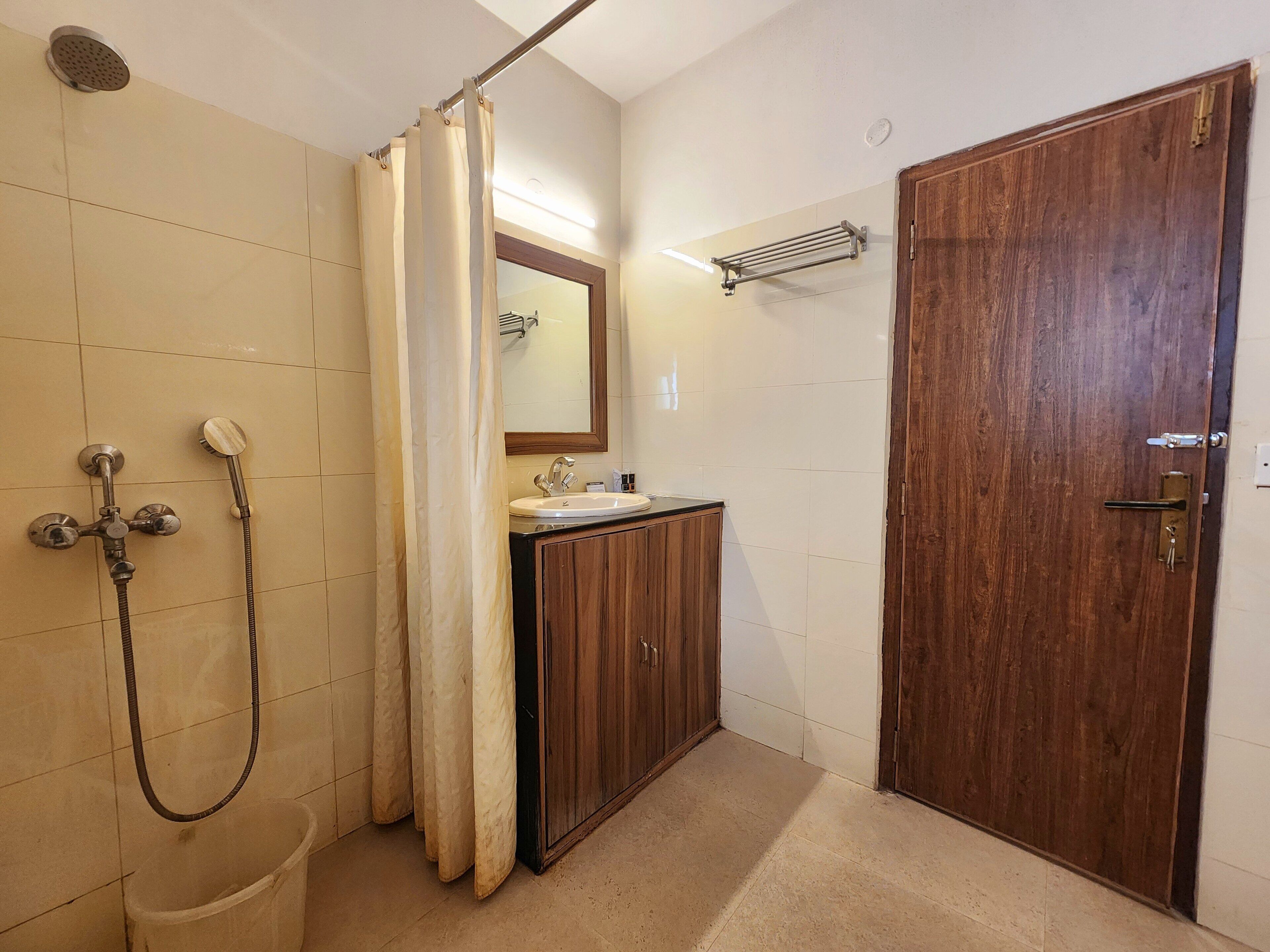Un baño con ducha, lavamanos, espejo y puerta de madera.
