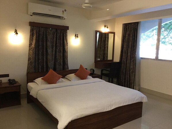 A hotel room with a bed, a desk, an air conditioner, and a window with curtains.