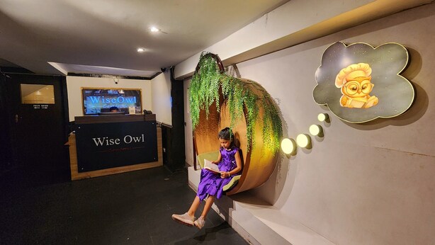 A child sitting on a wall with a large plant and a thought bubble illustration. - Wise Owl Comfotel (Kolkata)