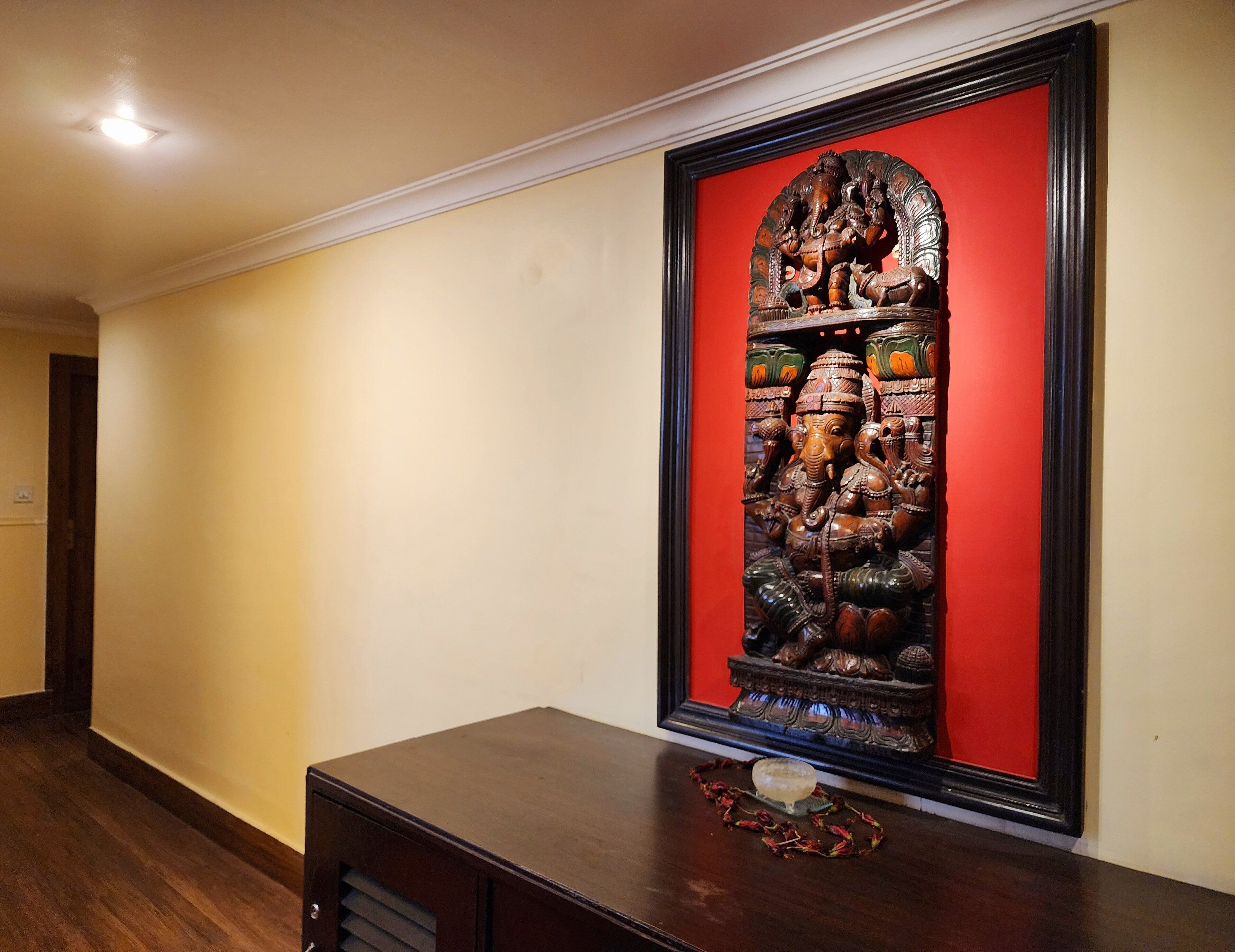 A hallway with a framed sculpture of a deity on a dark wooden table.