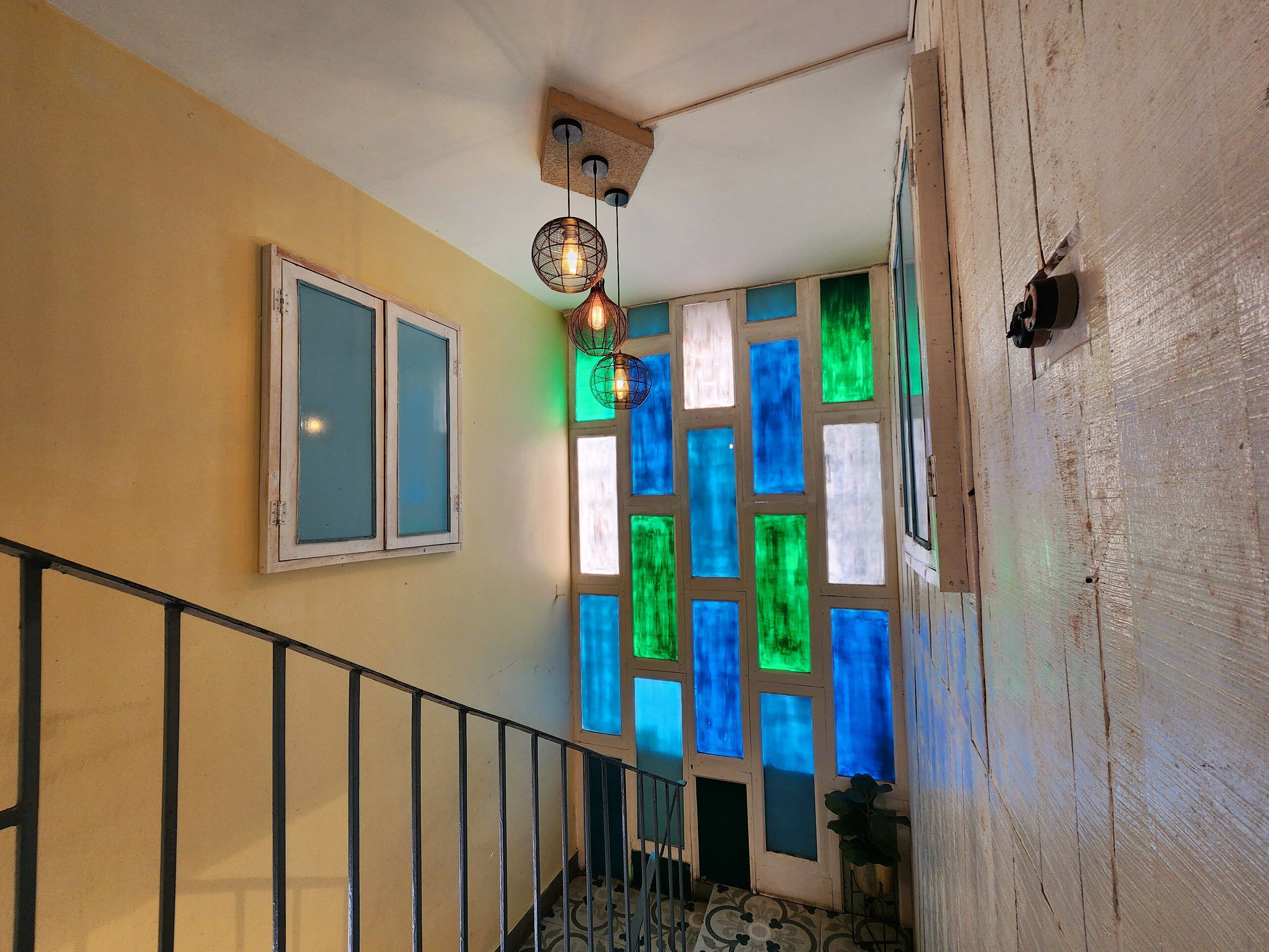 Eine Treppe mit Metallgeländer, ein Fenster mit satiniertem Glas und eine Wand mit farbenfrohen Glasfenstern.