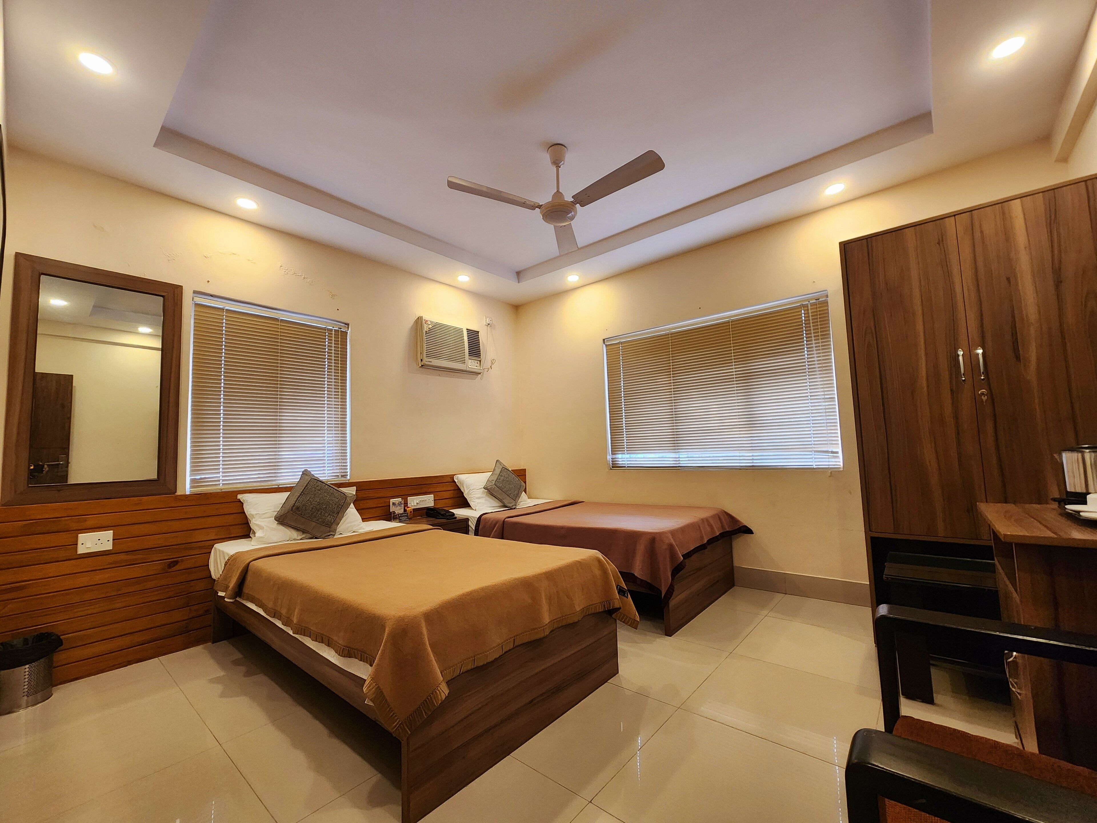 A hotel room with two beds, a ceiling fan, a wardrobe, and a small table.
