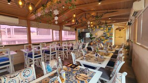 A restaurant with white tables and blue cushioned chairs, decorated with patterned tablecloths and various table settings. - Wise Owl Comfotel (Kolkata)