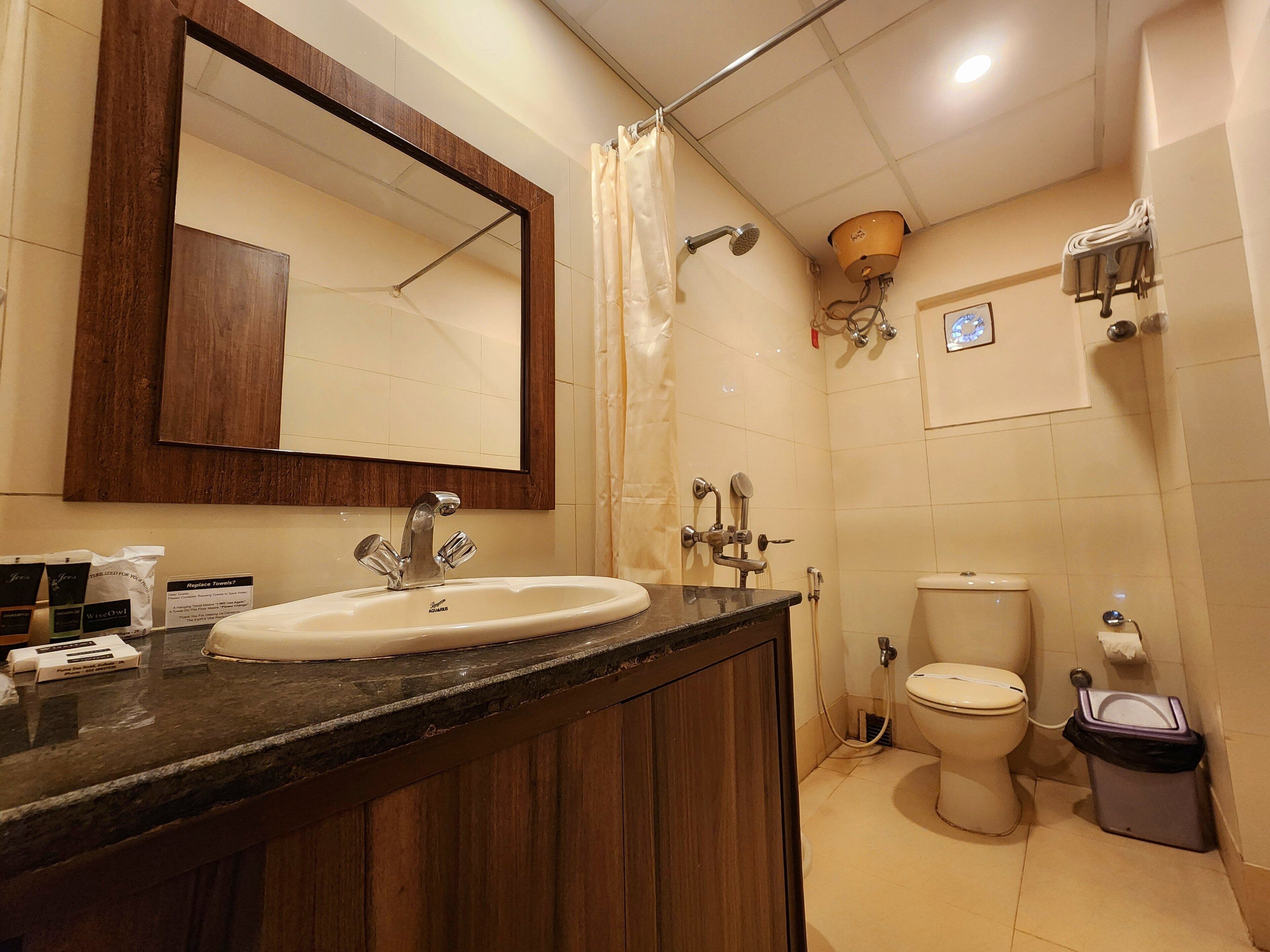 Un baño con tocador de madera, lavamanos, espejo, ducha e inodoro.